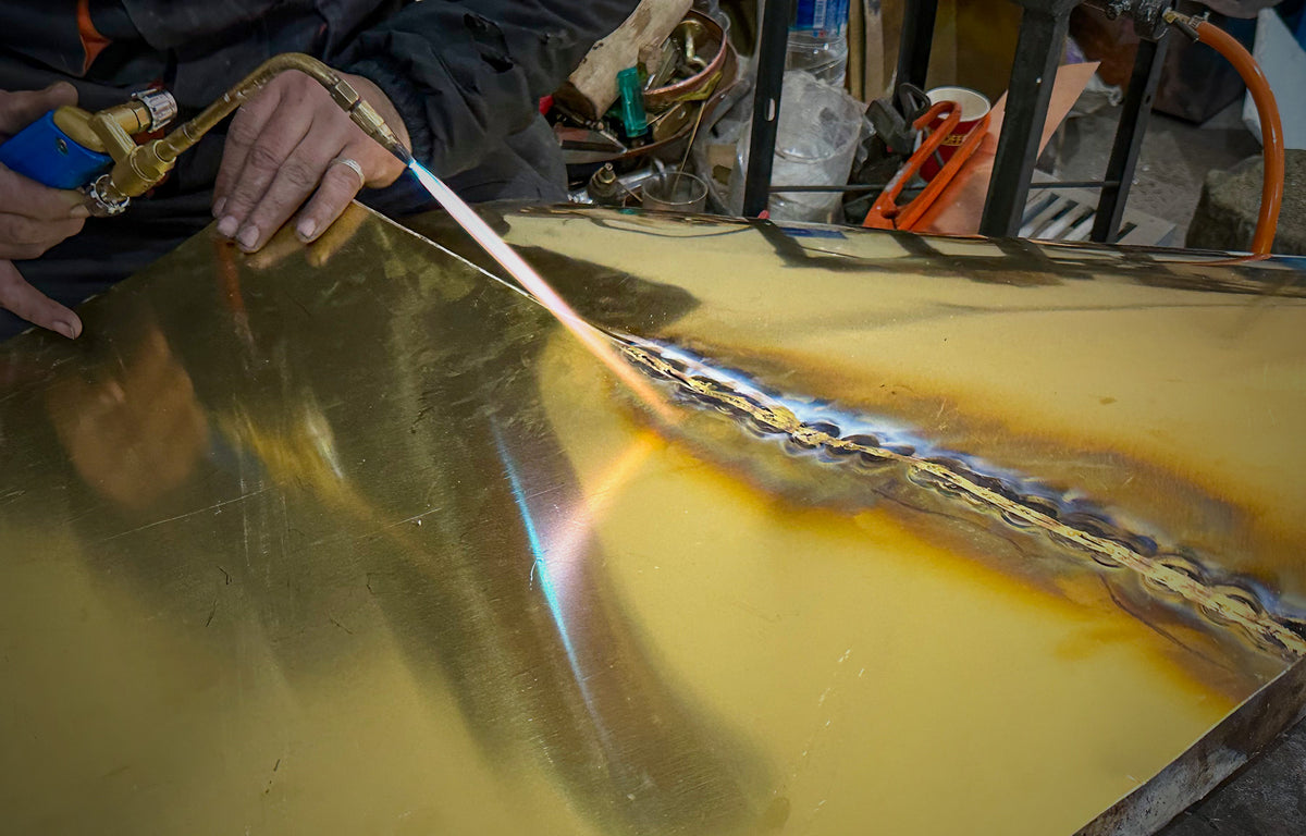 Coppersmith brazing a seam on a sheet of brass with a torch