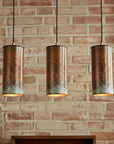 Three cylindrical pendant lights hanging against a brick wall.
