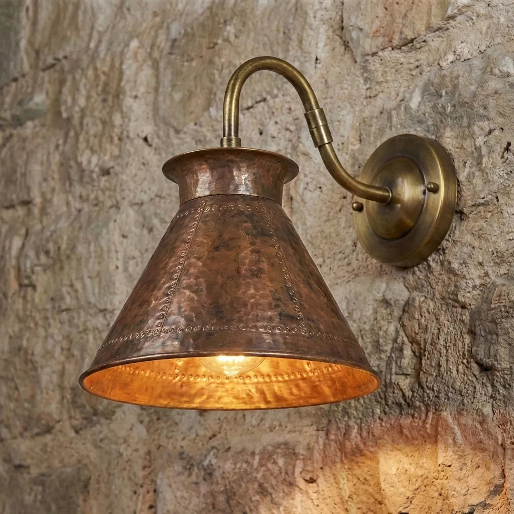 Handmade hammered copper wall sconce with brass arm mounted on stone wall