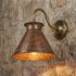 Handmade hammered copper wall sconce with brass arm mounted on stone wall