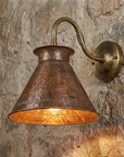 Handmade hammered copper wall sconce with brass arm mounted on stone wall