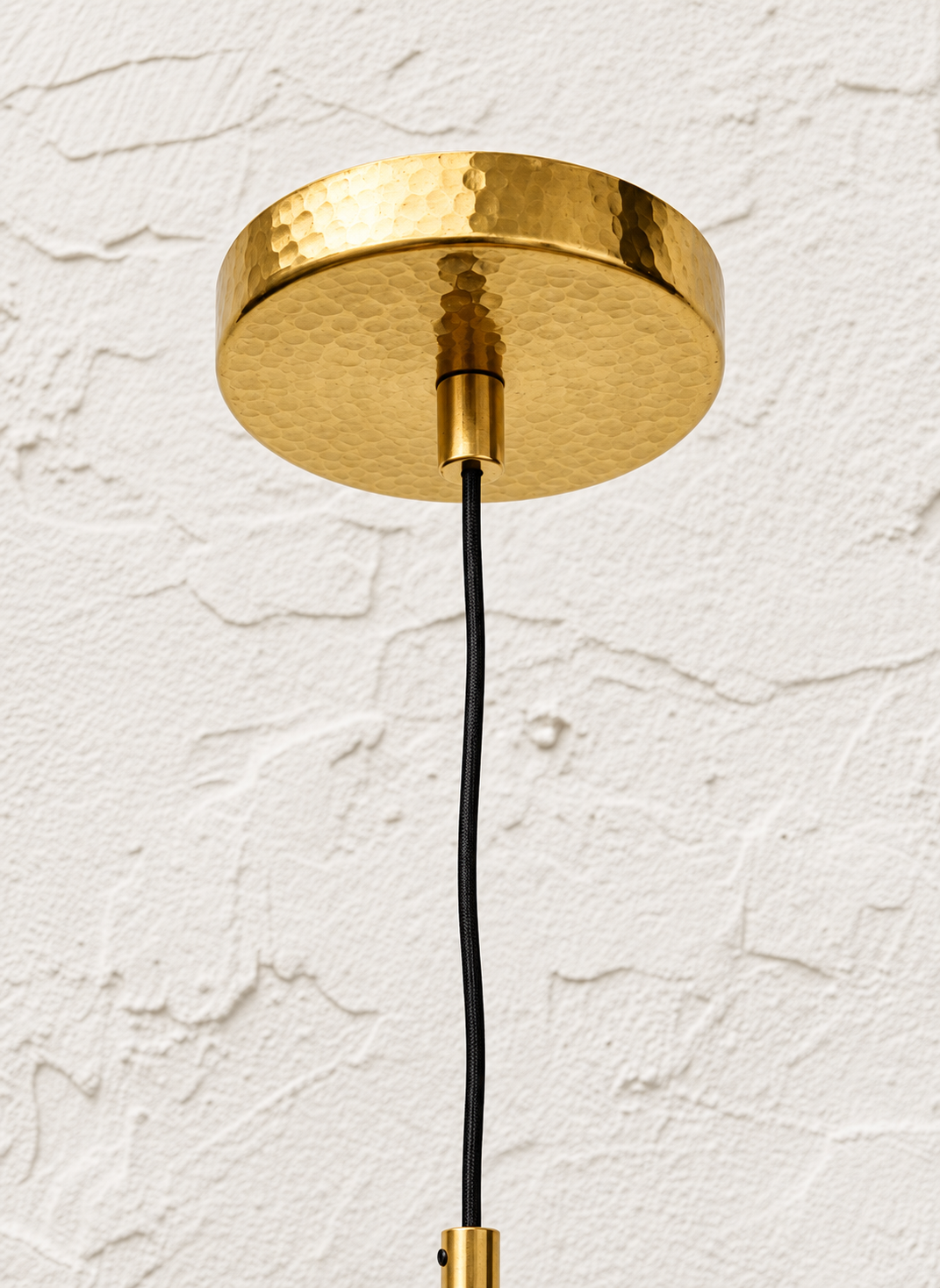 Hammered brass ceiling canopy and black cord detail for sculptural pendant light