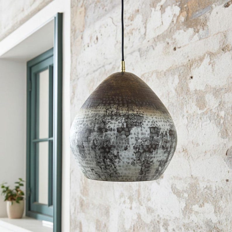 Oxidized copper dome pendant with textured patina beside a window