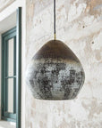 Oxidized copper dome pendant with textured patina beside a window
