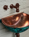 Aged-copper wall faucet above handcrafted green-patina copper sink